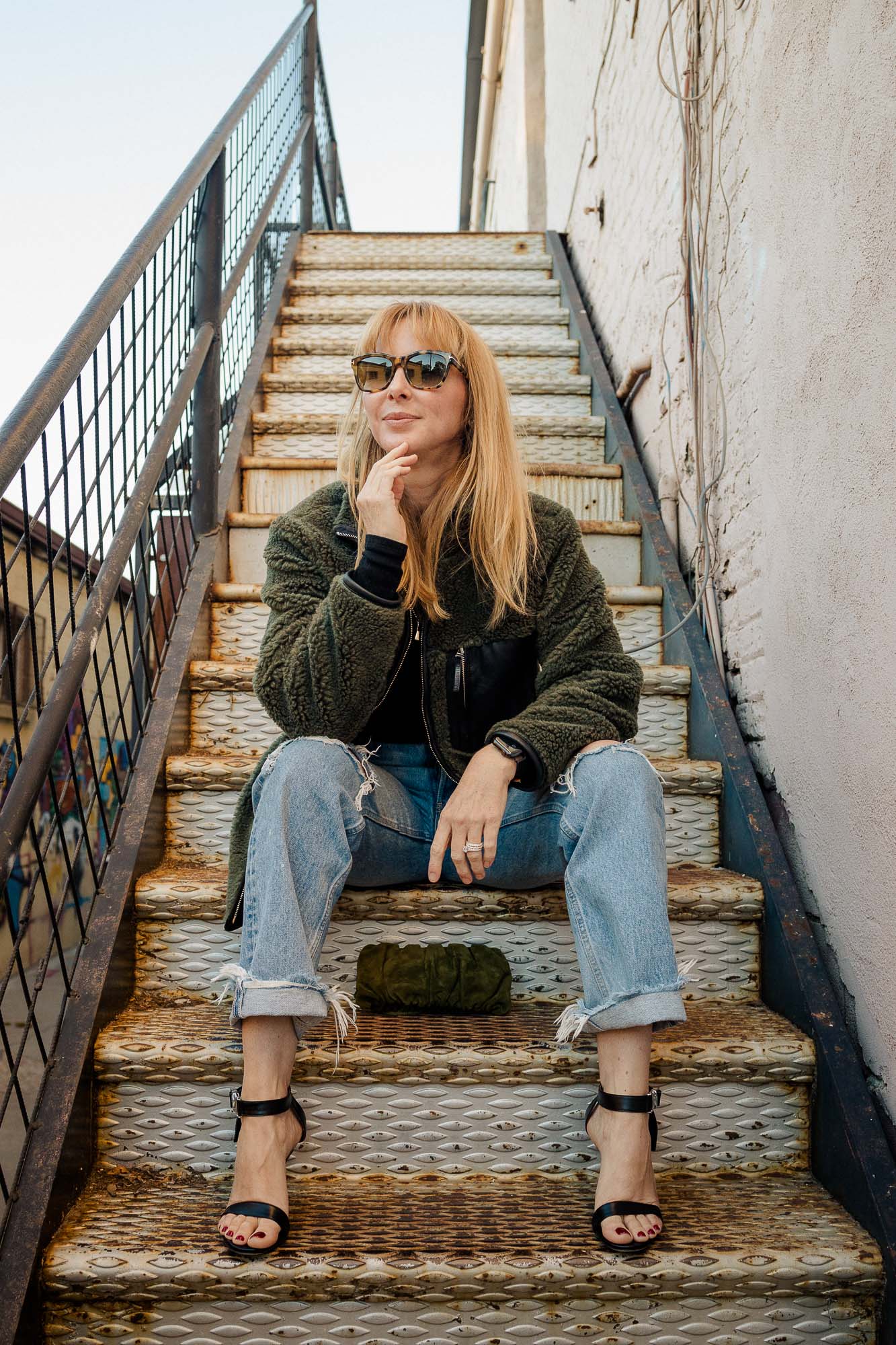 Sitting on steps wearing Staud black heels with Moussy Odessa jeans and the Anine Bing Ryder coat.