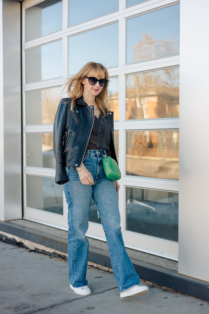 Wearing the KUT from the Kloth black and white polka dot blouse with Mother Tunnel Vision jeans, a black leather Iro jacket, green Clare V. bag and Axel Arigato clean 90s sneakers.