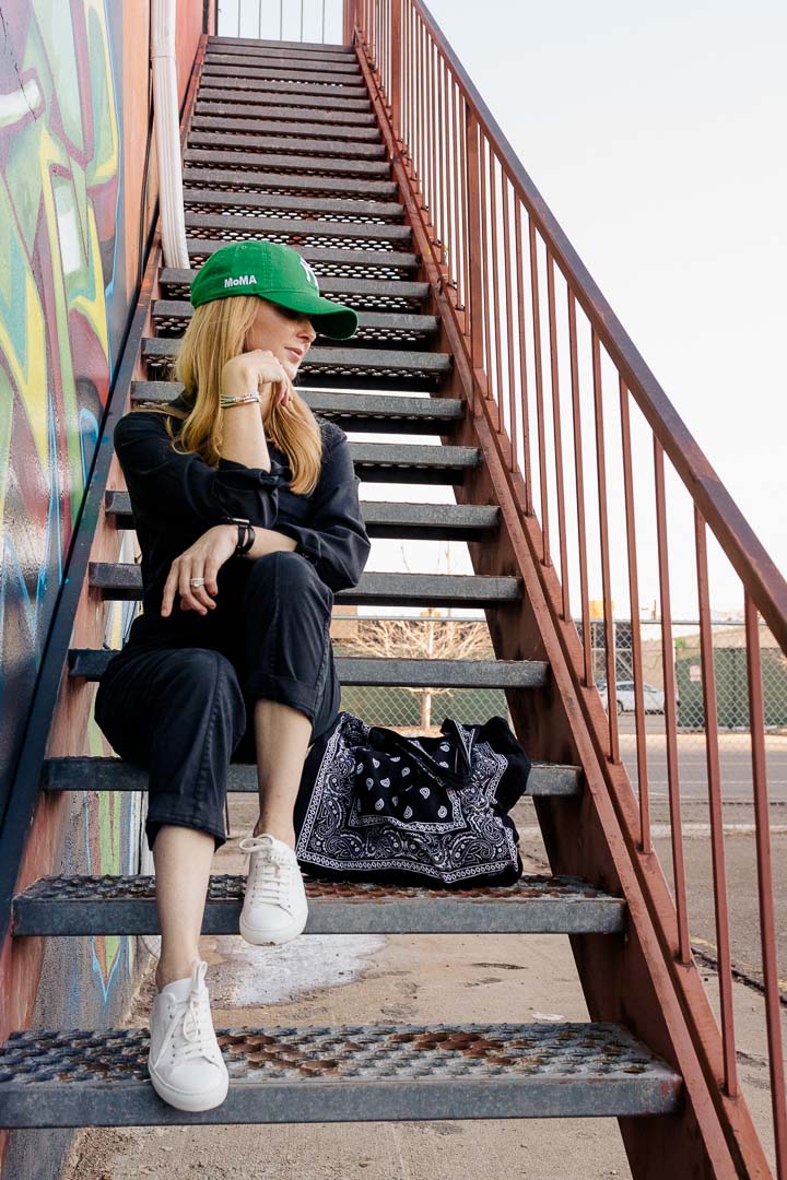 Wearing the Alex Mill Expedition jumpsuit in washed black with white Axel Ariagato sneakers and a green NY Yankees hat.