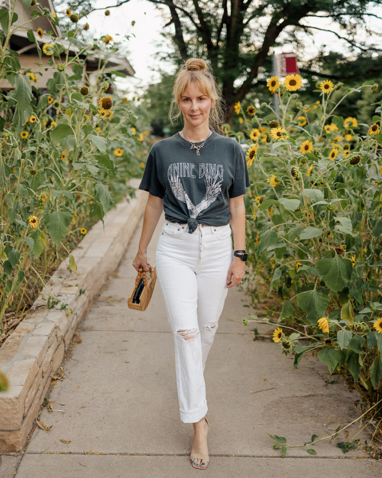 Wearing the Anine bing Lili graphic tee in washed black with white Agolde jeans in front of wild sunflowers.