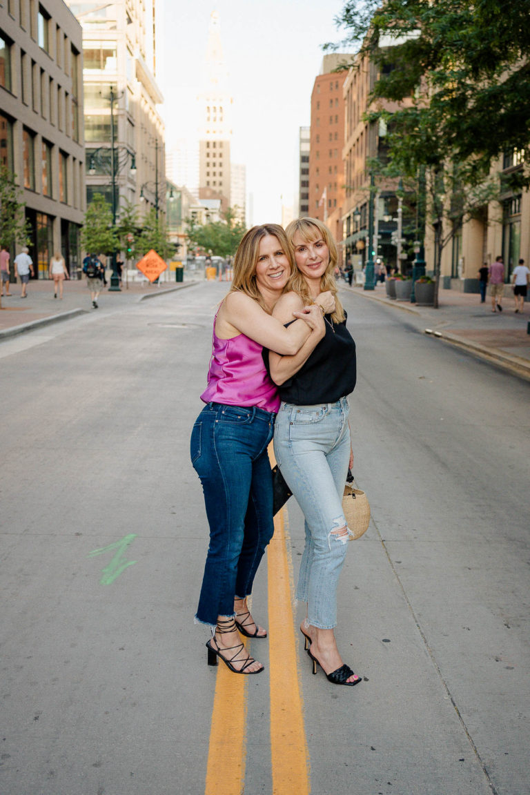 Tammy & Rachel in the street downtown Denver wearing a pink camisole and black off the shoulder top.