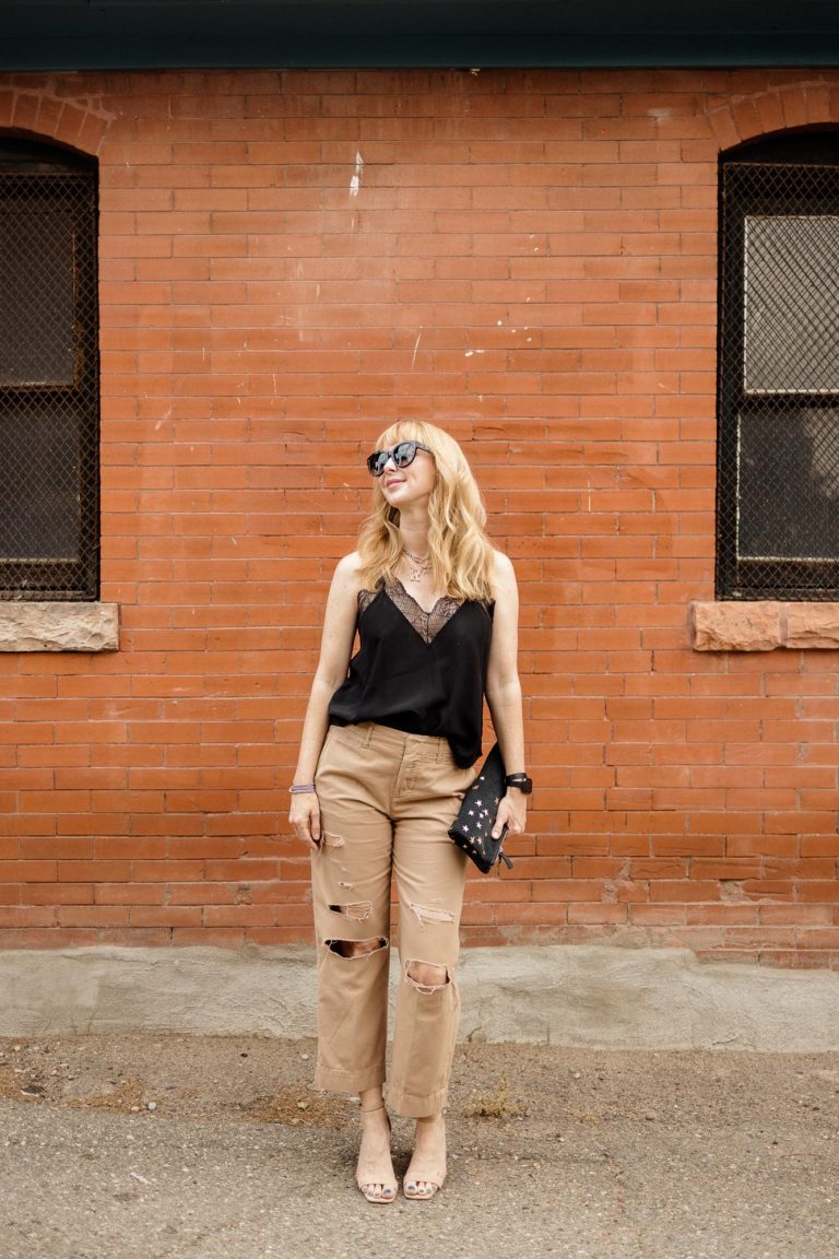 Wearing the Frame Le Tomboy ripped trousers in tan with a black Zadig et Voltaire silk camisole, nude heels and a Clare V clutch in front of a red brick wall.