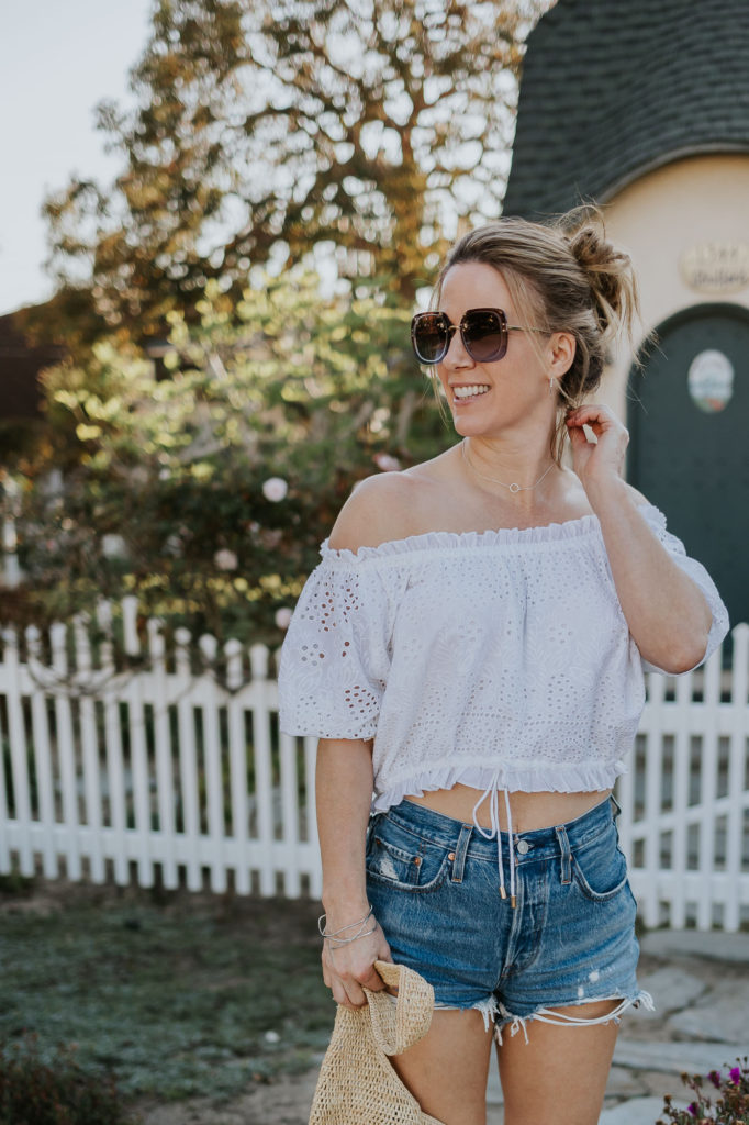 Girl in front of white picket fence in white top and denim shorts.