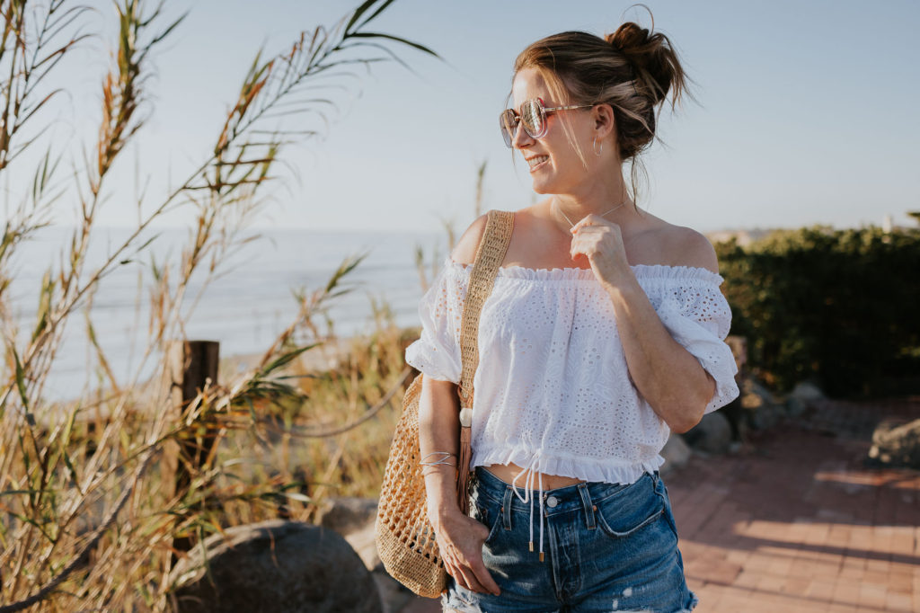 Beach in Encinitas California, wearing off the shoulder white top and cutoff shorts.