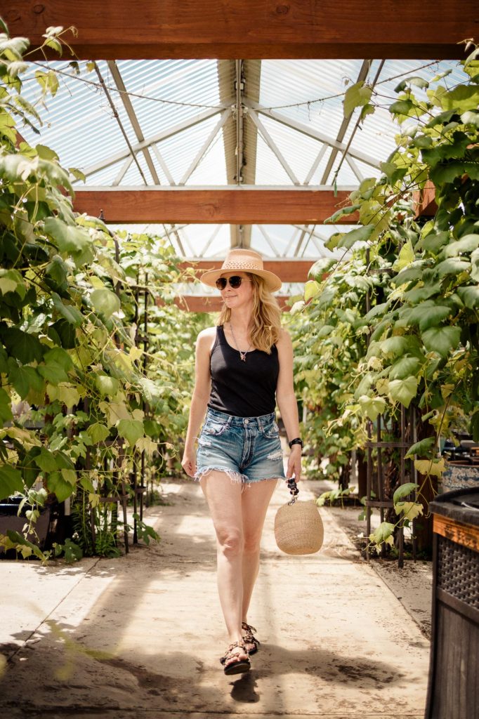 Wearing Moussy cutoff shorts, a black tank, sports sandals and a sun hat at the plant nursery for Friday Sale Finds.