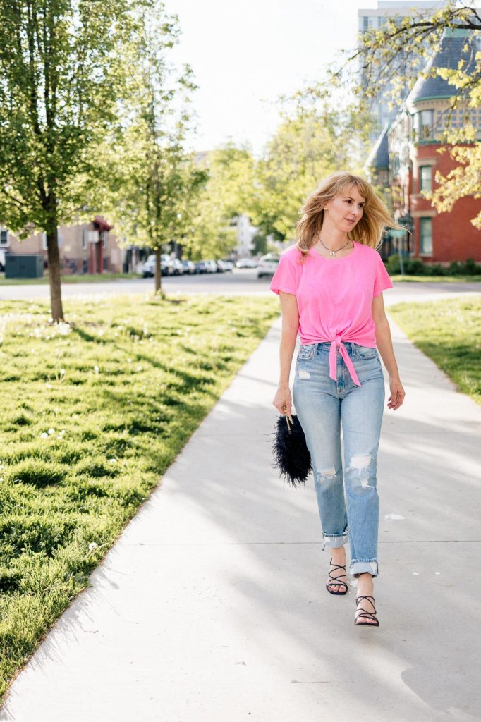 Walking down the sidewalk in a hot pink Sundry tee, distressed Mother jeans, black sandals and a feather bag.
