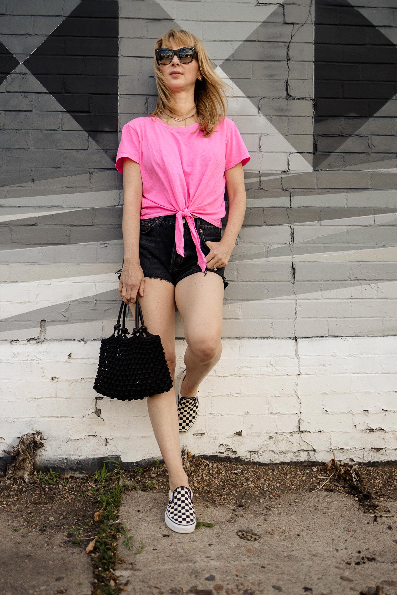 Wearing a hot pink Sundry tee and washed black shorts in front of a black and white mural.