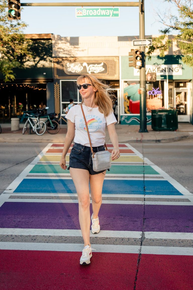 Walking across rainbow crosswalk in redone pride shirt, black cutoff shorts and retro sneakers.