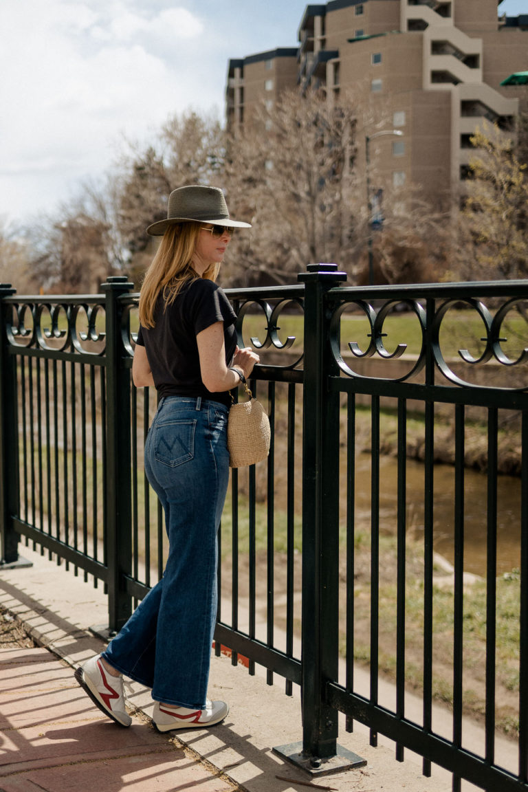 Standing by an iron fence wearing the Rag and Bone green packable fedora, red retro sneakers and MOTHER Roller Tomcat jeans.