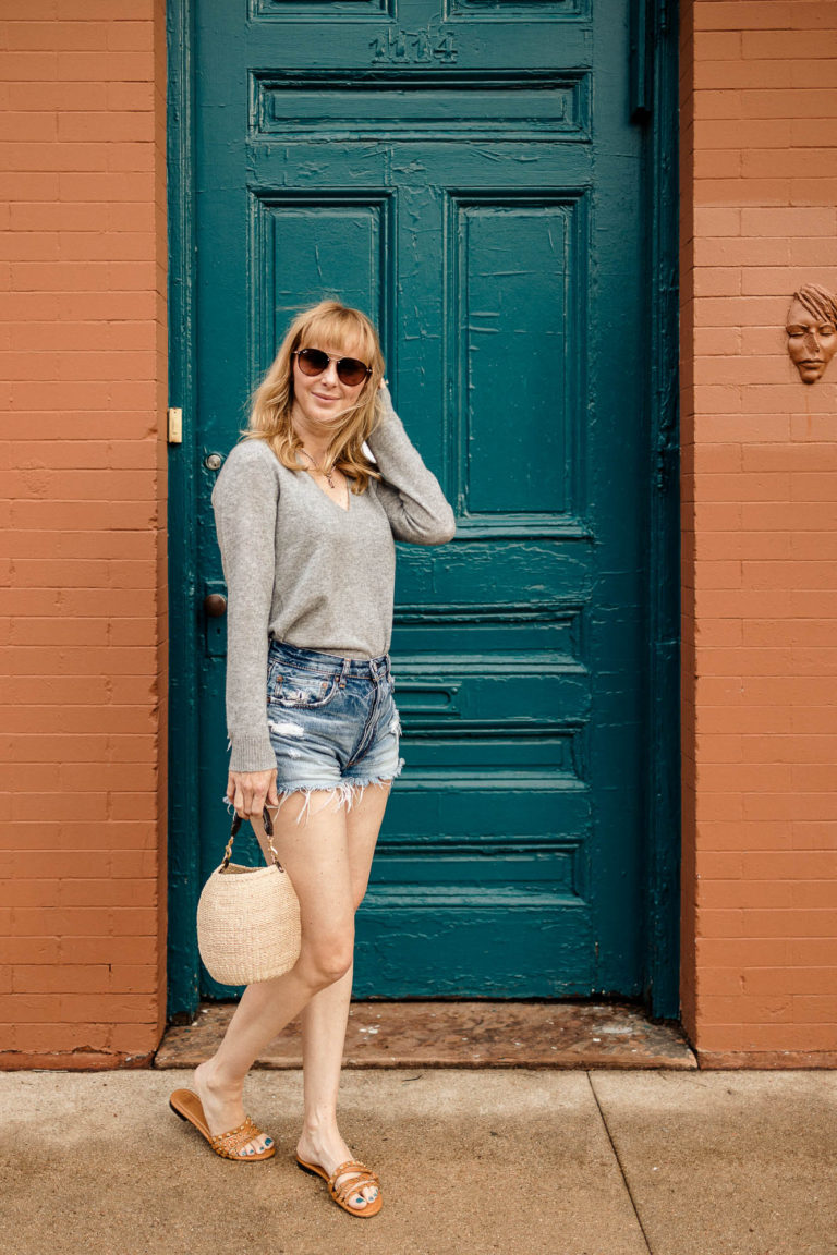 Wearing the gray Theory Adrianna cashmere sweater with Moussy cutoff shorts and the Clare V pot de miel in front of a teal door downtown.