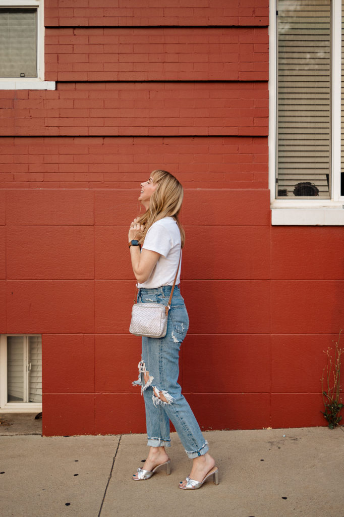 Wearing the Veronica Beard silver granita heels with my silver Clare V crossbody bag and Agolde 90s jeans in front of a red wall.