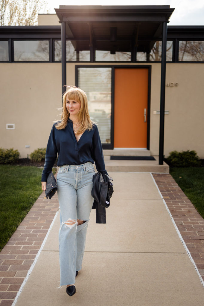 Wearing a Vince silk blouse in navy with ripped loose 90s jeans in front of a modern house with an orange door.