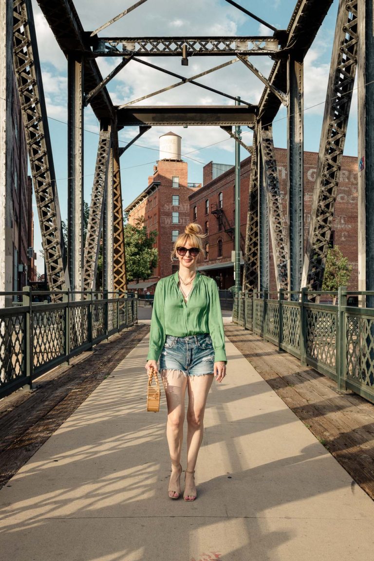 Wearing a green Zadig silk blouse with cutoff moussy shorts and nude heels on a bridge.